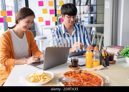 Les employés de l'équipe commerciale discutent du travail et préparent la pizza et la pomme de terre jetons pour partager le repas lors de la pause déjeuner pour de bonnes relations au bureau Banque D'Images