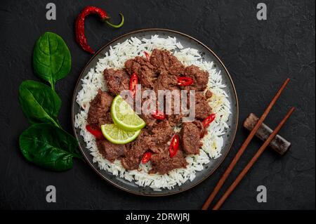 Bœuf Rendang sur une assiette noire au dessus de la table en ardoise noire. Indonésien padang cuisine plat de viande. Cuisine asiatique. Vue de dessus Banque D'Images