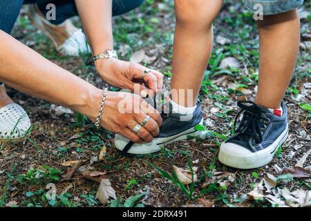 Maman noue des baskets à son petit fils. Vue rapprochée des mains des femmes et des félets d'un petit garçon debout sur l'herbe. Banque D'Images