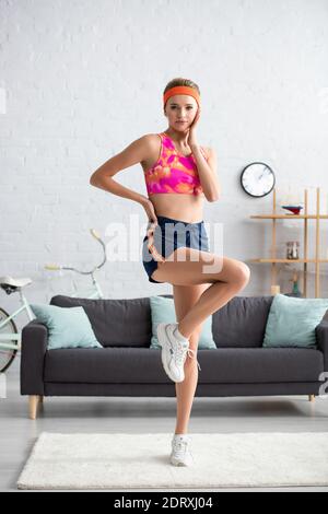 Pleine longueur de jeune sportswoman avec la main sur la hanche posant lorsque vous regardez l'appareil photo à la maison sur un arrière-plan flou Banque D'Images