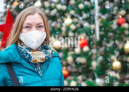 Une femme dans un masque de protection près d'un arbre de Noël à la décoration festive dans la rue. Noël et nouvel an pendant la pandémie du coronavirus. Banque D'Images