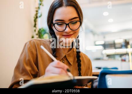 Une femme avec des lunettes écrit dans un carnet dans un café Banque D'Images