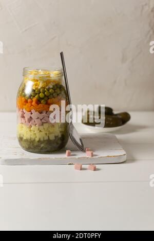 Ingrédients pour la salade russe Olivier dans un pot en verre avec une cuillère sur fond blanc. Cuisine russe. Copier l'espace. Banque D'Images