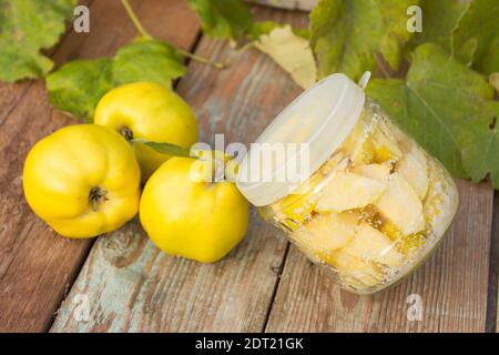 Fruits de coing mûrs sur fond de bois. Tranches de coing confites dans un pot en verre. Concept de conservation. Banque D'Images