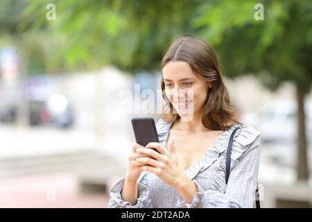 Bonne adolescente à envoyer des SMS sur un smartphone en marchant dans le rue Banque D'Images