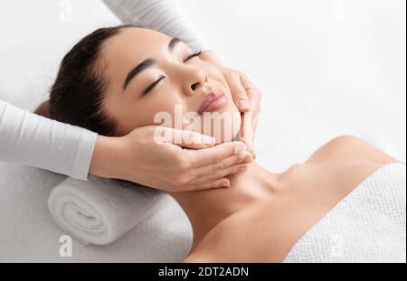 Massage du visage. Gros plan d'une femme asiatique attirante qui se fait soigner de beauté au spa Banque D'Images