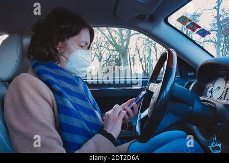Francfort, Allemagne. Décembre 2020. Femme naviguant sur un téléphone portable depuis le siège du conducteur. Vue de profil. Banque D'Images