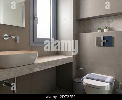 Intérieur de style contemporain de petite salle de bains moderne carrelée de pierre de galet grise avec fenêtre, lavabo de bateau, WC mural caché accroché Banque D'Images