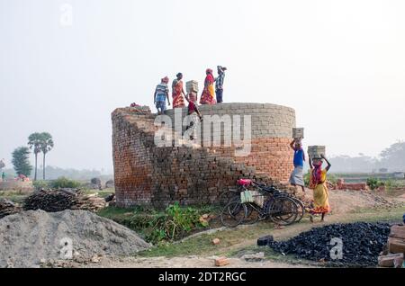 Photo d'un four en brique dans le quartier isolé de Hooghly. Les hommes et les femmes adultes travaillent dur pour arranger les briques brutes dans le four à cuire. Banque D'Images