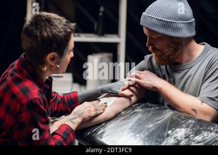 Jeune fille informelle tatouage artiste met un bandage avec vaseline sur la main d'un jeune homme après avoir appliqué avec succès un tatouage sur sa main Banque D'Images