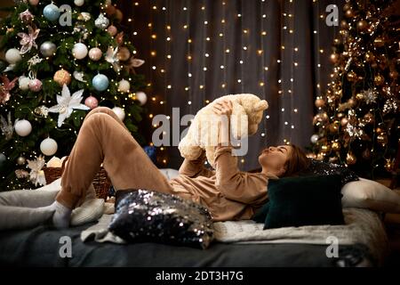 bonne jeune femme tient l'ours en peluche contre les lumières de bokeh, arbre de noël. Atmosphère chaleureuse. Banque D'Images