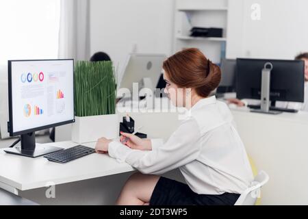 Fille Manager dans un chemisier blanc à l'ordinateur calcule le profit et la perte de l'entreprise, construit des tableaux Banque D'Images