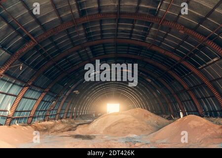 Grand hangar oblong avec des piles de sable pour l'industrie et la construction. Banque D'Images