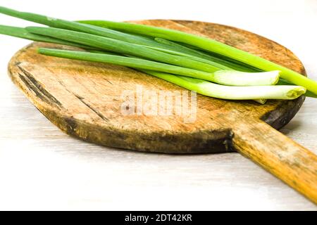 Plumes d'oignon de printemps vert sur l'ancienne planche à découper en bois sur fond de table blanc Banque D'Images