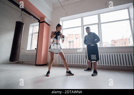 Combat d'entraînement des kickboxers masculins et féminins. Des coups de pied et des coups de pied sur la patte de boxe. Travail par paires Banque D'Images