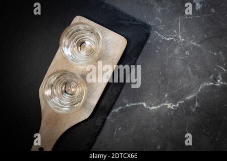 Deux verres avec vodka sur une planche en bois. Sur fond de pierre grise Banque D'Images