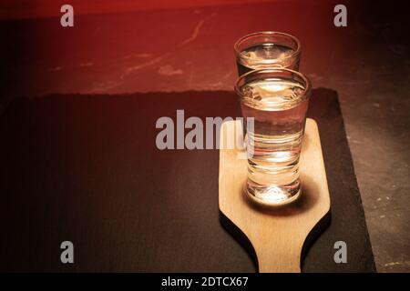 Deux verres avec vodka sur une planche en bois. Sur fond de pierre grise Banque D'Images