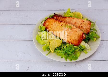 Saumon fraîchement cuit dans un plat avec salade et citron sur fond de bois blanc. Banque D'Images