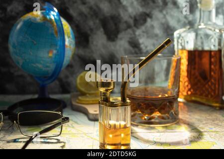 Globe avec une carte sur la table. Carafe avec whisky cognac sur la carte. Points et loupe sur la carte. Banque D'Images