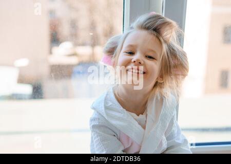 portrait d'une petite fille gaie dans les cheveux curlers on l'arrière-plan de la fenêtre Banque D'Images