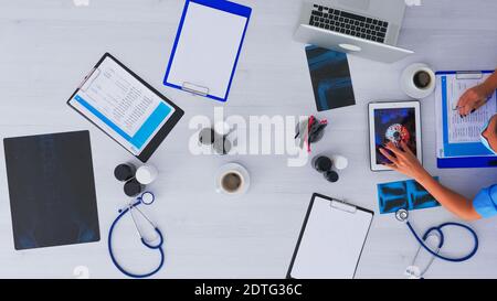 Vue de dessus d'un médecin qui recherche sur le virus à l'aide d'une tablette, prend des notes assis sur le bureau dans une clinique médicale avec des rayons X et la technologie numérique. Assistant d'écriture sur le presse-papiers, espace de copie, concept de mise à plat. Banque D'Images