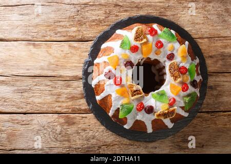 Gâteau fraîchement cuit avec raisins secs, abricots séchés, cerises séchées, kiwis et canneberges et glaçage en gros plan sur une planche sur la table. Vue horizontale du dessus Banque D'Images