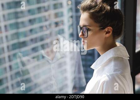 Jeune femme d'affaires debout à côté de la grande fenêtre. Bureau dans un bâtiment moderne de la grande ville Banque D'Images