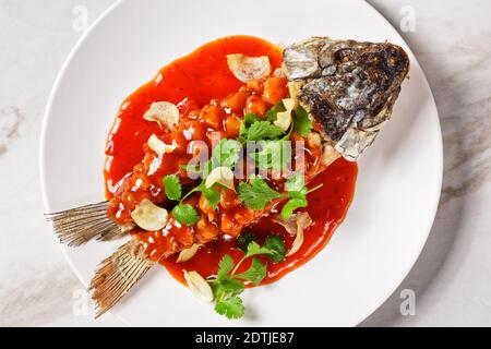 Cuisine chinoise : écureuil de carpe ou songshu yu sous une sauce aigre-douce et de la coriandre fraîche servie sur une assiette blanche sur un fond de pierre de marbre blanc, à Banque D'Images