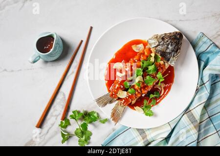 Cuisine chinoise : écureuil de carpe ou songshu yu sous une sauce aigre-douce et de la coriandre fraîche servie sur une assiette blanche sur un fond de pierre de marbre blanc, à Banque D'Images