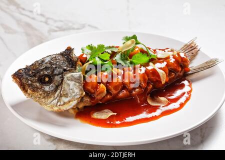 Cuisine chinoise : écureuil de carpe ou songshu yu sous une sauce aigre-douce et de la coriandre fraîche servie sur une assiette blanche sur un fond de pierre de marbre blanc, à Banque D'Images