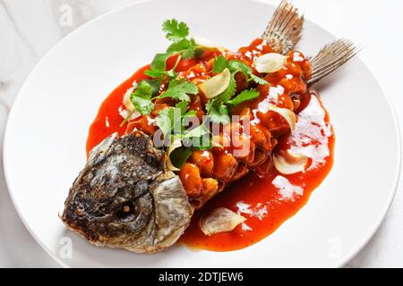 Cuisine chinoise : écureuil de carpe ou songshu yu sous une sauce aigre-douce et de la coriandre fraîche servie sur une assiette blanche sur un fond de pierre de marbre blanc, à Banque D'Images