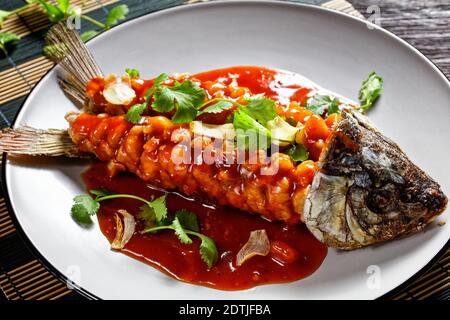 Écureuil de carpe : poisson aigre et doux chinois avec coriandre fraîche et ail séché sur une assiette grise sur une table en bois sombre, vue du dessus, cl Banque D'Images