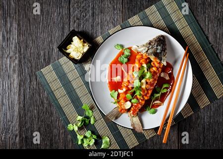 Écureuil de carpe : poisson aigre et doux chinois avec coriandre fraîche et ail séché sur une assiette grise sur une table en bois sombre, vue du dessus, cl Banque D'Images