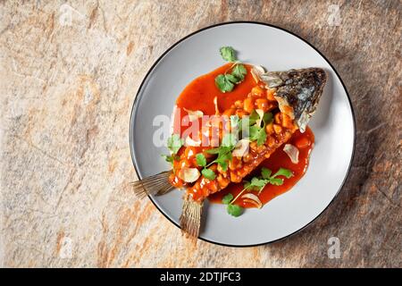 Poisson aigre-doux chinois, écureuil ou songshu yu sous une sauce aigre-douce, nappée de coriandre fraîche, servie sur une assiette sur fond de pierre, Banque D'Images