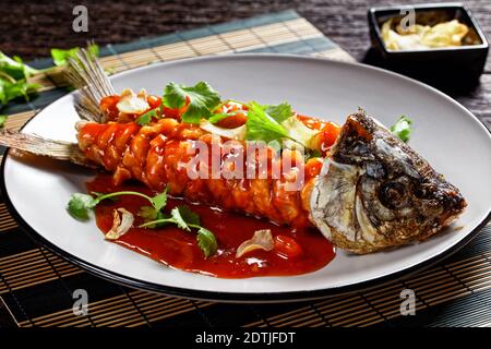 Écureuil de carpe : poisson aigre et doux chinois avec coriandre fraîche et ail séché sur une assiette grise sur une table en bois sombre, vue du dessus, cl Banque D'Images