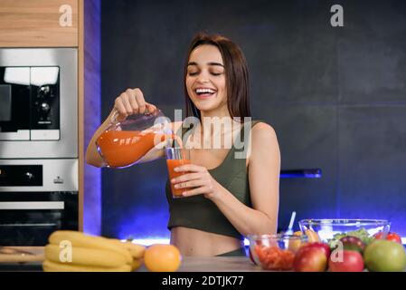 Une jeune femme verse du jus frais dans un verre dans une cuisine moderne et élégante. Banque D'Images