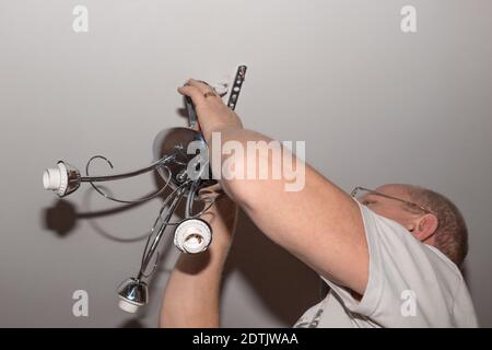 homme adulte avec des lunettes à la maison porte un lustre du plafond. Amélioration et rénovation des locaux. Banque D'Images