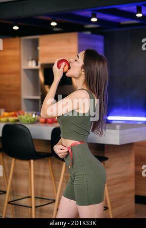 Jolie jeune femme savourant une pomme dans la cuisine après un délicieux petit déjeuner sain. Mode de vie sain et concept végétarien. Banque D'Images