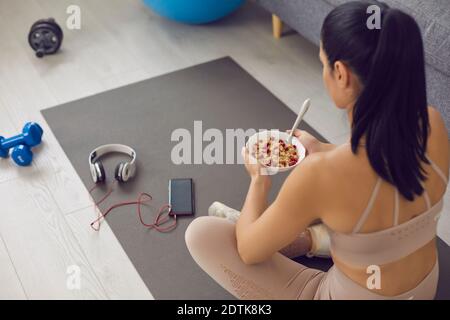 Femme se détendant sur un tapis de fitness et ayant un en-cas sain après entraînement sportif à la maison Banque D'Images