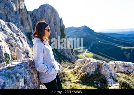 Attention sélective de la jeune femme caucasienne debout sur une montagne pic avec un regard dans le vide avec un panorama magnifique en arrière-plan et contre-jour effe Banque D'Images