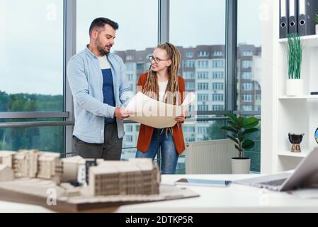 Un homme à barbe plein de confiance et sa collègue féminine avec des dreadlocks analysant un projet imprimé sur papier. Banque D'Images