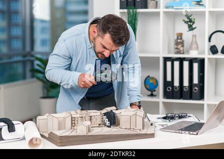 L'inspecteur d'architecte examine un modèle de maison à l'aide d'une loupe. Inspection de maison et concept immobilier. Banque D'Images