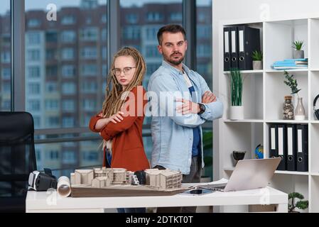 L'architecte professionnel se tient dos à dos avec une jolie femme collègue avec des dreadlocks dans le studio de design. Banque D'Images