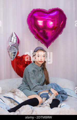 Une adolescente s'assoit sur le lit le jour de la Saint-Valentin entouré de ballons. Photo de haute qualité Banque D'Images