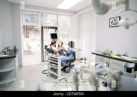 Cabinet du dentiste moderne. Mère et petite fille ayant un contrôle régulier et parlant avec leur dentiste, jeune femme africaine. Soins buccaux, caries Banque D'Images