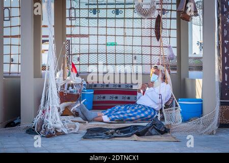 Pêcheur arabe, réparant filet de pêche maison et yacht en bois, portant un masque facial et s'assoit sur le sol du boam traditionnel Banque D'Images