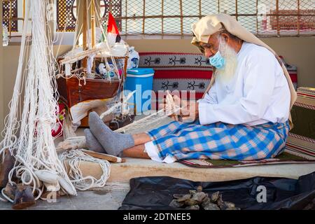 Pêcheur arabe, réparant filet de pêche maison et yacht en bois, portant un masque facial et s'assoit sur le sol du boam traditionnel Banque D'Images