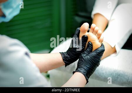 Esthéticienne en gants de protection en caoutchouc faisant un massage sur la semelle du pied féminin dans un salon de beauté spa Banque D'Images