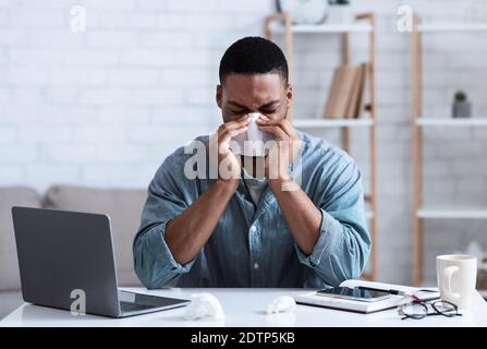 Sick Black Guy Blowing Nose à Napkin travaillant au bureau Banque D'Images