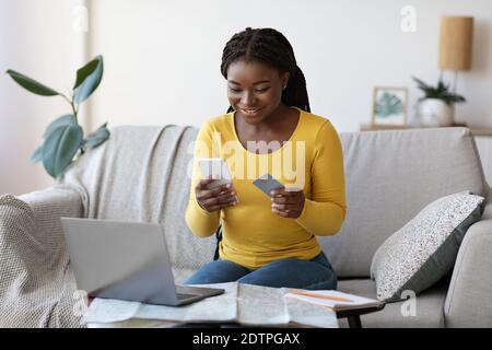 Black lady réservant des billets en ligne avec un smartphone et une carte de crédit à la maison Banque D'Images